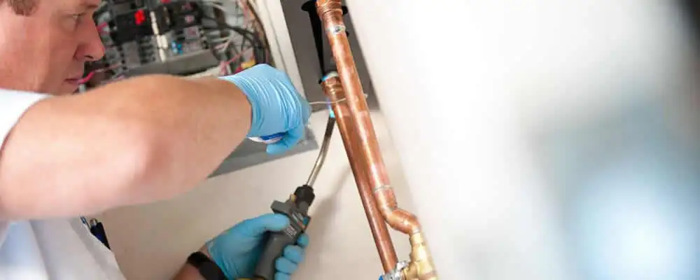 Water heater repair technician testing copper pipe connections and controls in Kenosha, WI